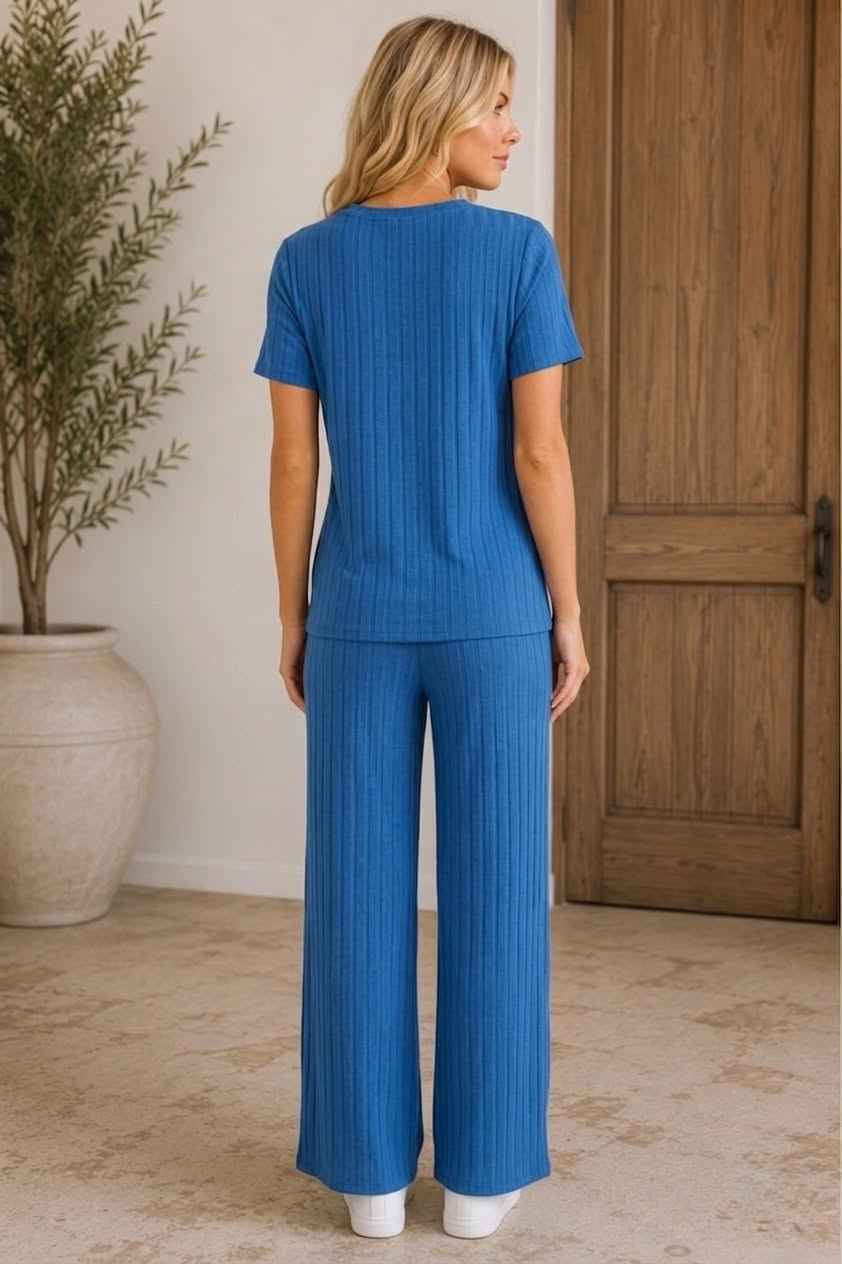 Woman wearing a blue outfit standing in a room with a wooden door and plant.