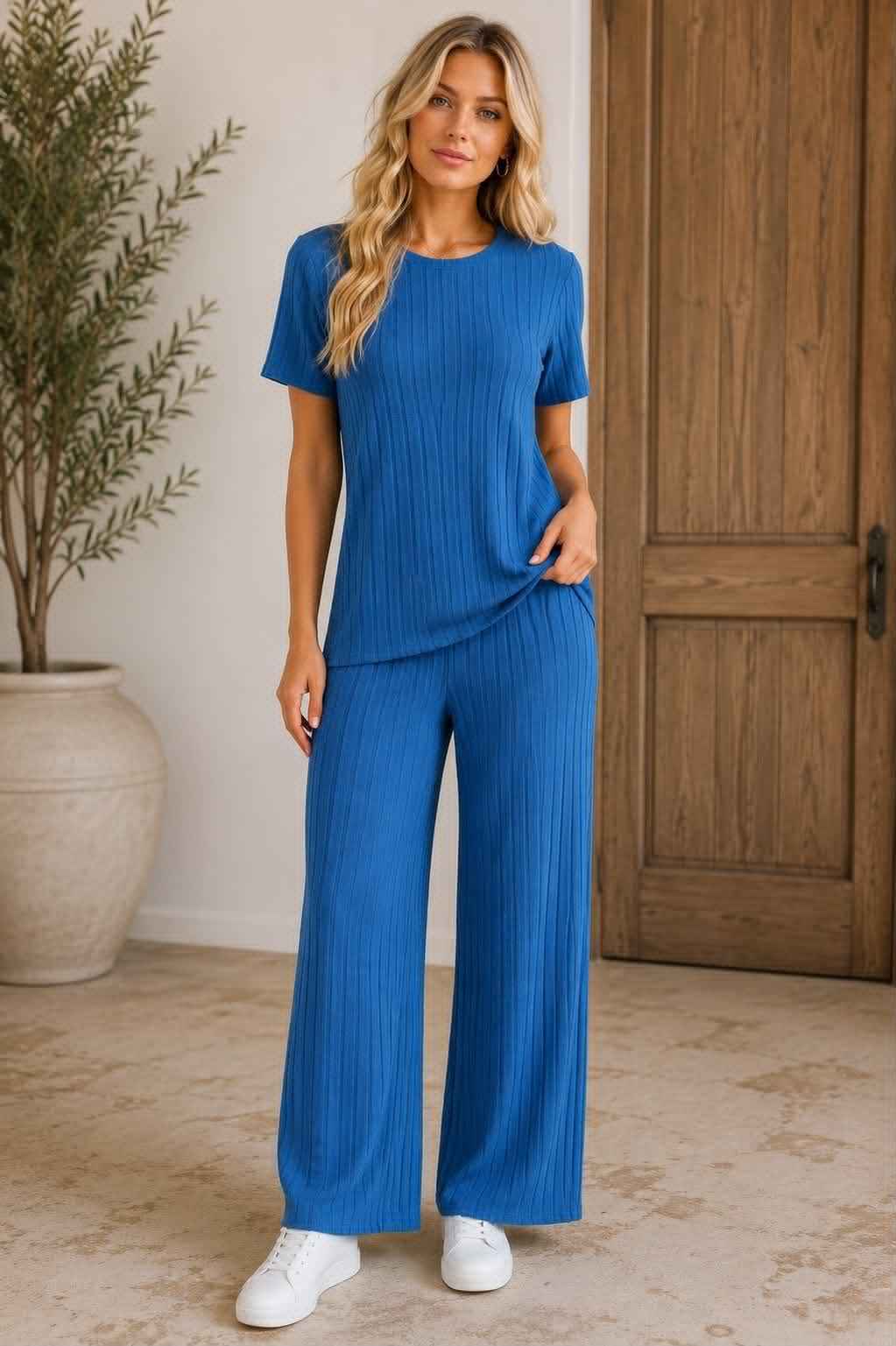 Woman wearing a blue outfit standing in a room with a wooden door and plant.