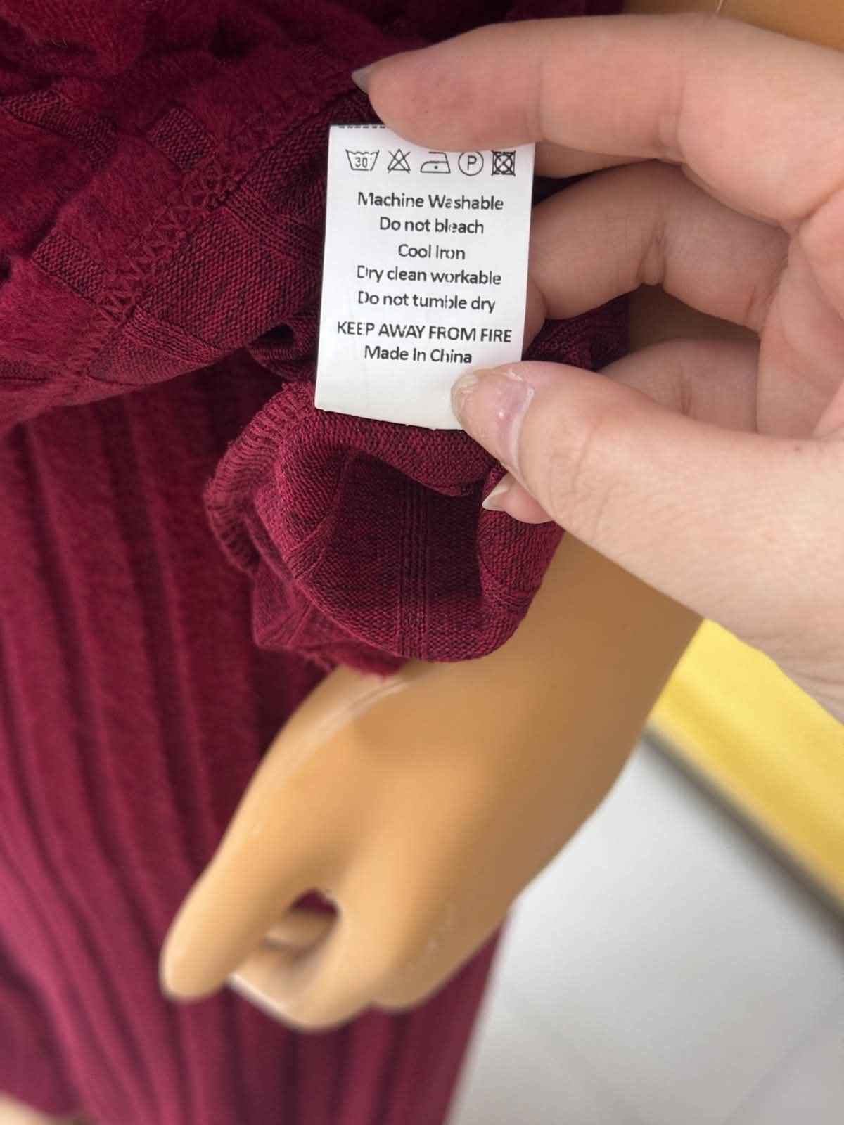 Hand holding a clothing label on a maroon garment with a blurred background